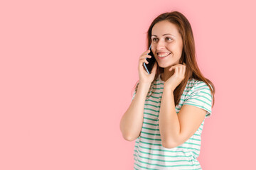 Portrait of a happy brunette girl talking on a mobile phone and smiling, isolated on a pink background.