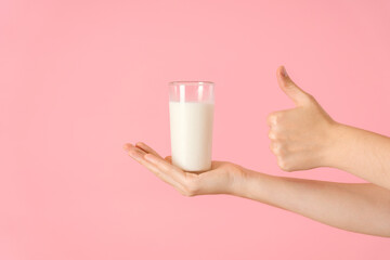 A hand with a glass of milk on a pink background. A glass with a dairy product on an open palm and...