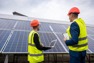 young worker in overalls with boss in overalls looking at newly installed solar panels.