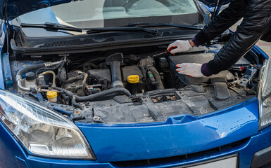 a man in gloves looks under the hood of an open car for a breakdown.