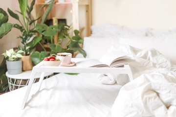 Breakfast in bed. Heart shaped white plate with fresh strawberries, cup of coffee, book and plants flowers. Still life composition. Mother, Valentine day concept.
