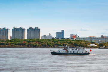 Chinese pleasure boat on the Amur River in autumn against the background of buildings in Heihe,...
