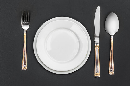 Plates with fork, knife and spoon on black background. Top view.