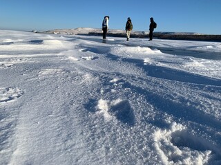 three people walking on the ice of the Volga river through the snow in winter