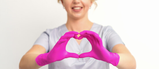A smiling caucasian woman doctor wearing pink gloves in uniform showing the symbol of a heart against a white background - Powered by Adobe