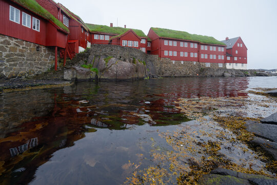 Thorshavn, Faroe Islands - 05.29.2017: Red wooden houses with white windows in the government district of Thorshavn, Faroe Islands. Reflection in water surface. Rainy, day.