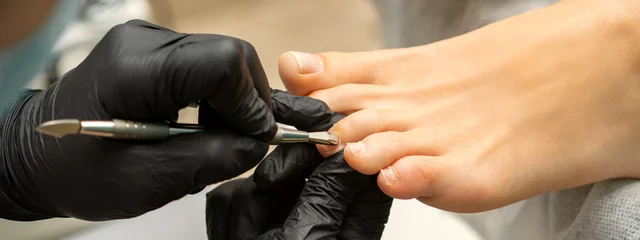 Wall murals Pedicure Cuticle Removal on Toes. Hands in black gloves of pedicure master remove cuticle on female toes by pusher