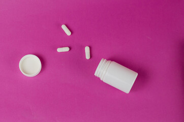 Open White plastic vial and three medicine pills against a magen
