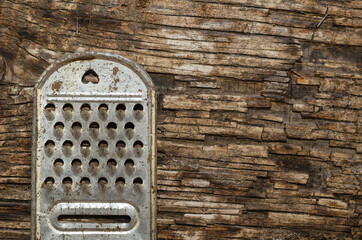 An old rusty kitchen grater on a rotting board with a knot.