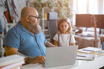 Bearded father looks at little girl taking part in video lesson via laptop at home