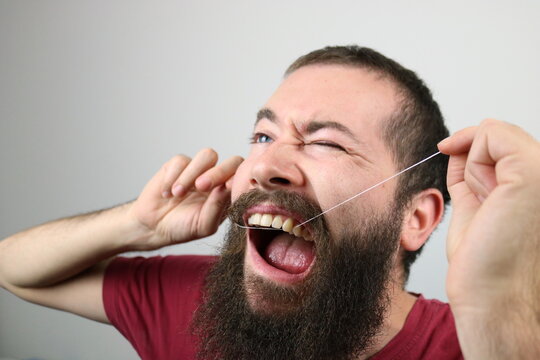 Bearded man removes bacteria, plaque and food from between teeth. Using dental floss. 