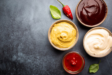 Classic set of sauces, American yellow mustard, ketchup, barbecue sauce, mayonnaise on black stone background, top view with copy space.