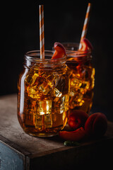 Glass of peach or apricot iced tea with fruit slices against dark blue background