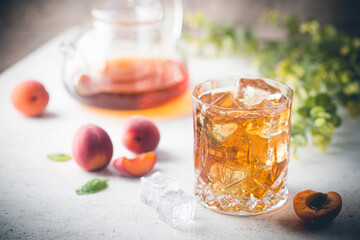 Glass of peach or apricot iced tea with fruit slices against white background