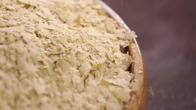 Nutritional brewers yeast flakes falling on a full rustic wooden bowl in slow motion. Macro. Rotation. Natural dietary supplement