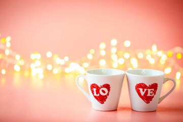 Valentines day concept with white coffee cups with love text and lights of garland over pink background
