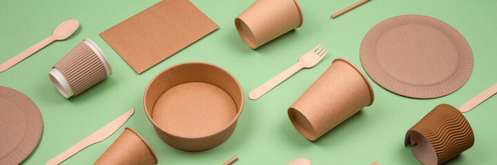 Banner with set of different eco-friendly tableware and kraft paper food packaging on green...