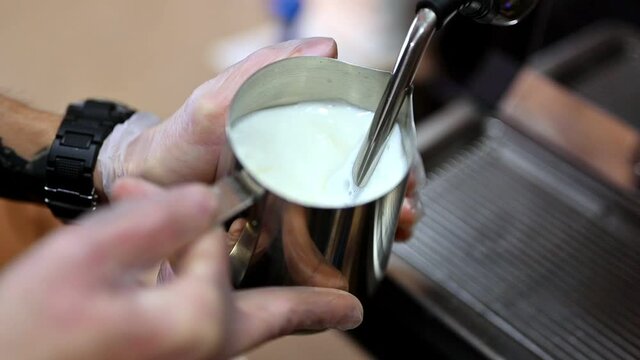 Crop barista steaming milk for coffee