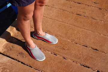 Protective neoprene shoes for coral and stones at sea. Aquashoes slippers for walking on corals. Legs of man in gray slippers, shoes for stones beach which protect foot on shore of pebbly beach sea
