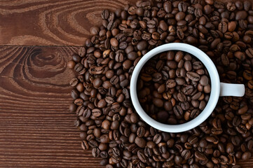 white cup filled with coffee beans on coffee background. Coffee beans on wooden table. Flat layout with top view. Copy space