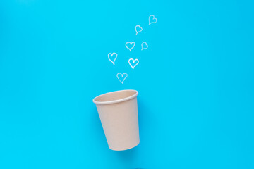 Ein nachhatliger Wegewerfbecher mit kleinen weißen Herzen auf einem blauen Hintergrund. Draufsicht, Kaffeeliebe.