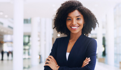 Cropped portrait of an attractive young businesswoman smiling and standing in the office with her arms crossed during the day - obrazy, fototapety, plakaty