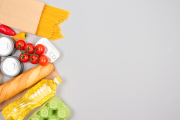 Food donations on light gray background with copy space - pasta, fresh vegatables, canned food, baguette, cooking oil. Food donation and food bank concept. Selective focus