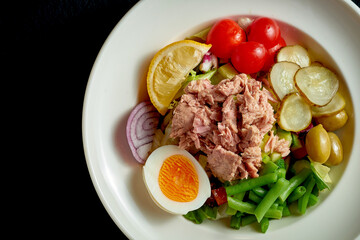 Diet nicoise salad with tuna, egg and asparagus in a white plate on a black background