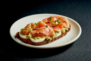 Toast with salmon and avocado mousse in a white plate on a black background