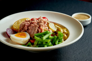 Diet nicoise salad with tuna, egg and asparagus in a white plate on a black background