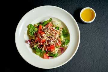 Diet salad with tomatoes and cucumbers, seeds in a white plate on a black background