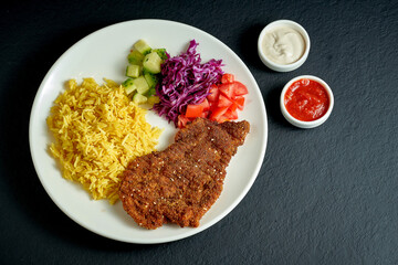 Chicken austrian schnitzel with rice and vegetables in a white plate on a black background