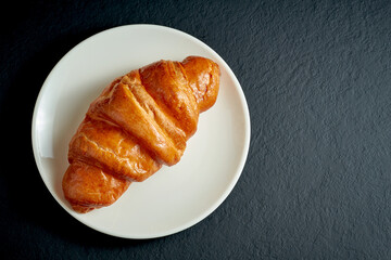 Creamy sweet croissant in white plate on black background
