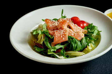 Diet salad with tomatoes and salmon in a white plate on a black background