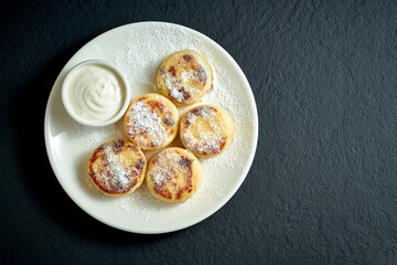 Cheesecake pancake with sour cream in a white plate on a black background. Syrniki