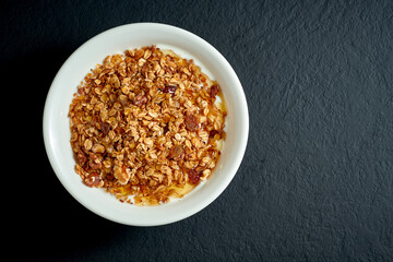 Healthy breakfast - granola with honey and yogurt in a white plate on a black background