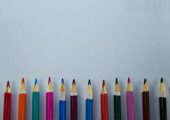 Colored pencils lie along a white sheet of paper. Copy space on a sheet of paper. Abstract background of colored pencils