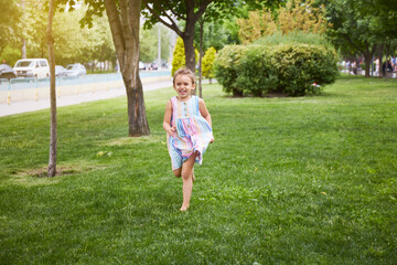 Happy girl running by grass while in colourful dress. Playing in park. Enjoying summer