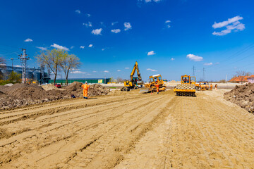 Road roller with spikes and earthmovers are working at construction site