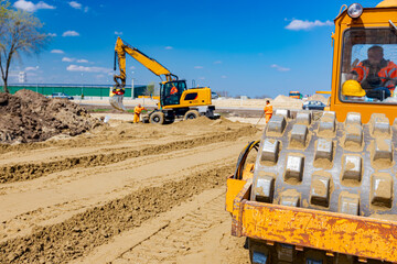 Road roller with spikes and earthmover are working at construction site