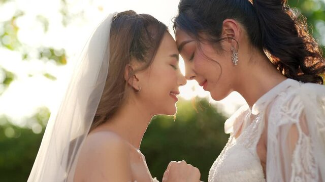 Portrait of Beautiful Asian woman lesbian couple in wedding dress holding hands walking together in the garden. Diversity sexual equality, lgbtq pride, marriage equality and Same-sex marriage concept