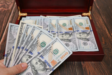 Cash dollars is  in hand on the background of a brown chest full of dollar bills. Focus on the money bill. - 478099796