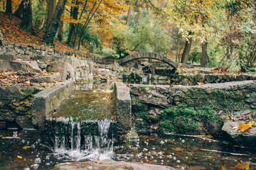 Beautiful autumn park with yellow leaves fallen. Beautiful autumn background landscape with stone bridge across the stream. Colorful foliage falling. Selective focus