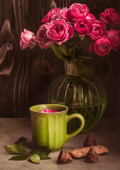 Coffee in a green mug, a bouquet of red roses in a glass vase on a dark background. Romantic stylish composition for a greeting card