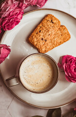 A mug of coffee with milk surrounded by roses. A morning gift and a good mood for a woman