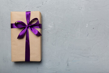 Holiday gift box wrapped in craft paper with colored bow on table background. Top view, flat lay,...