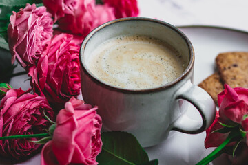 A mug of coffee with milk surrounded by roses. A morning gift and a good mood for a woman