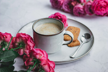 A mug of coffee with milk surrounded by roses. A morning gift and a good mood for a woman