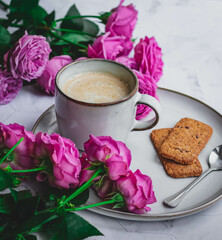 A mug of coffee with milk surrounded by roses. A morning gift and a good mood for a woman
