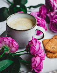 A mug of coffee with milk surrounded by roses. A morning gift and a good mood for a woman